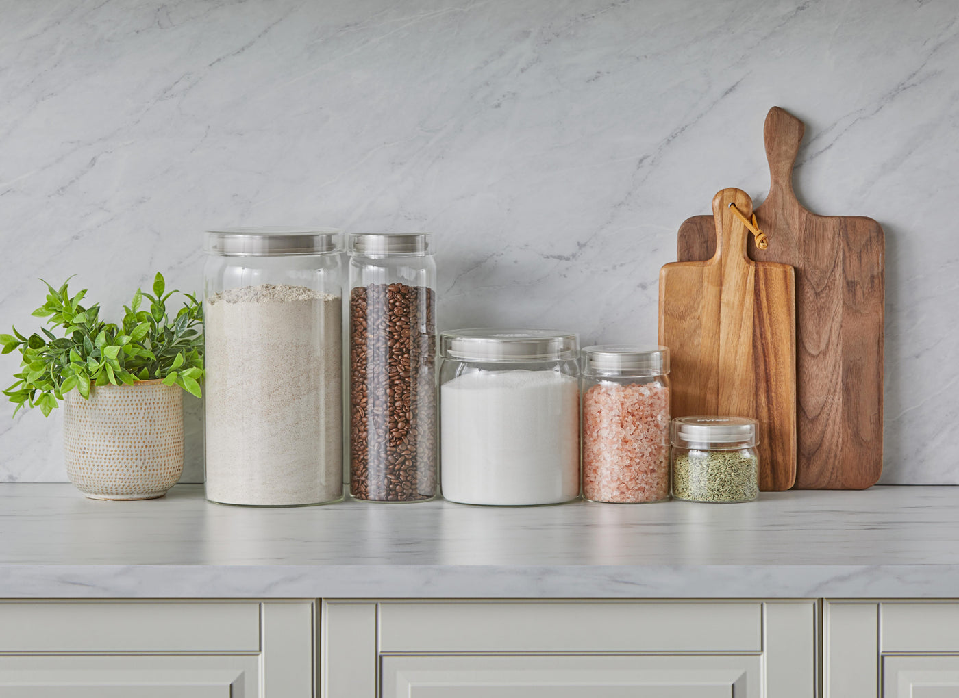 Kitchen counter with jars of spices and wooden cutting boards against a marble wall.