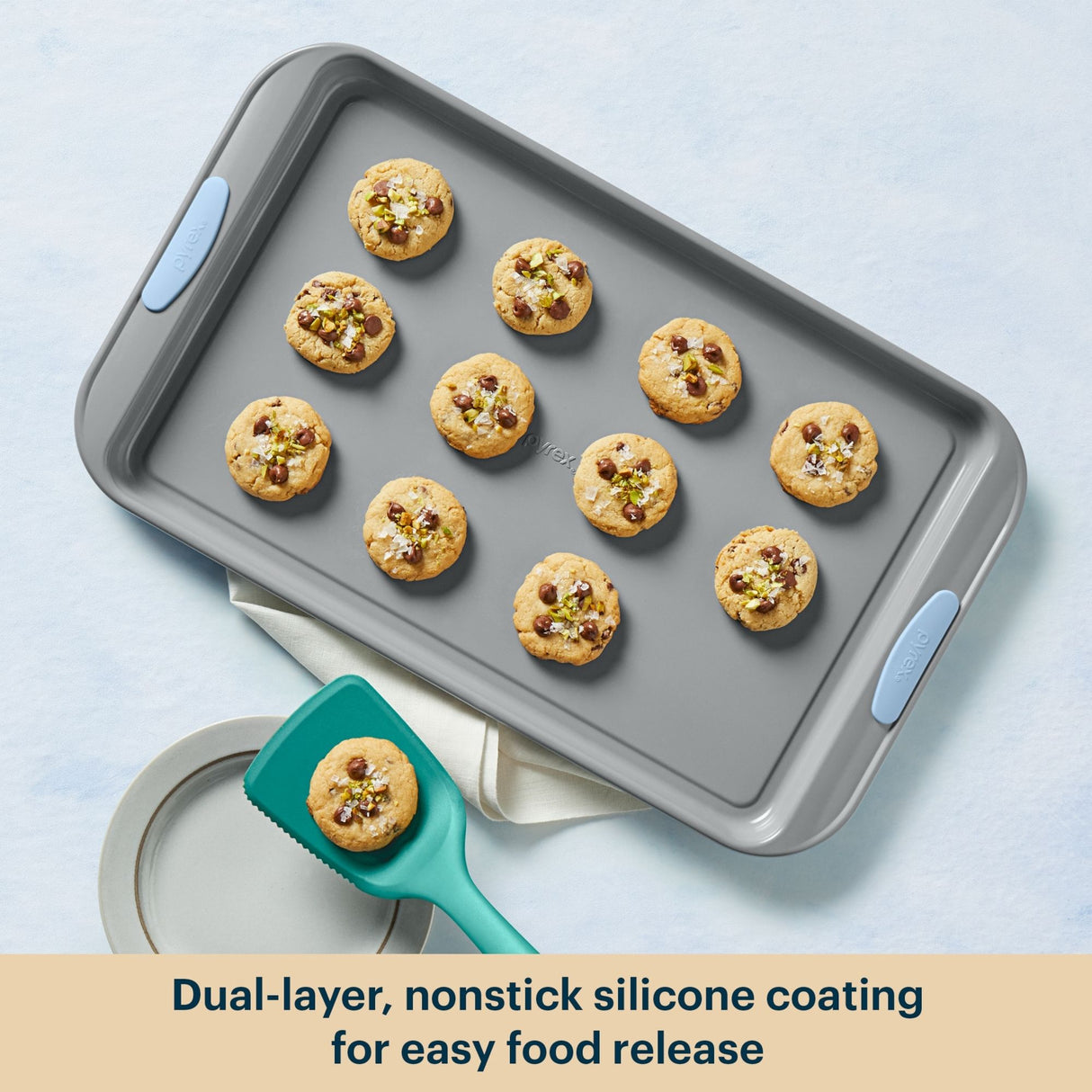 Gray baking tray with cookies and a green spatula on a light blue background