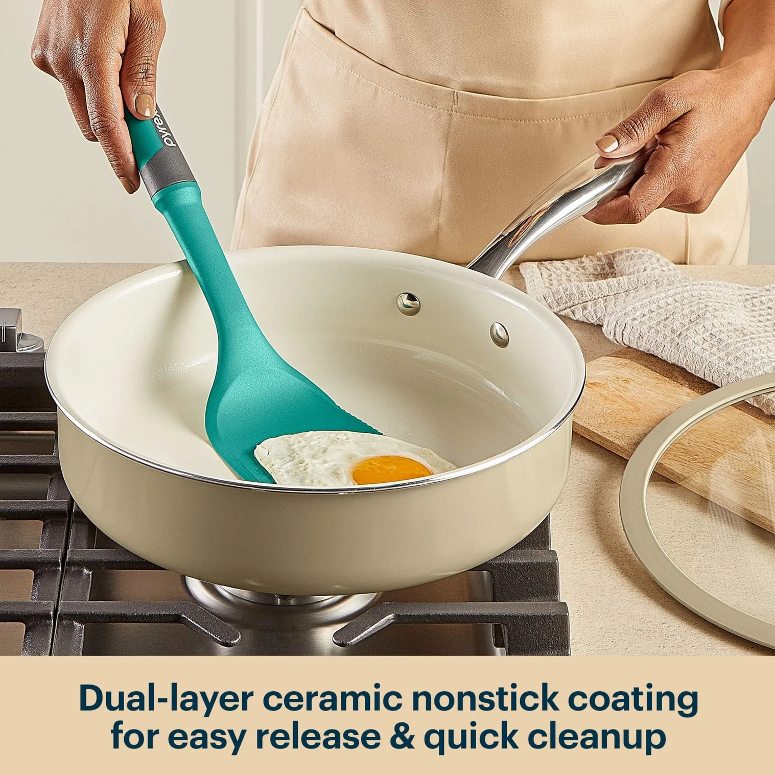Person using a green spatula to stir eggs in a beige ceramic nonstick frying pan on a stove.