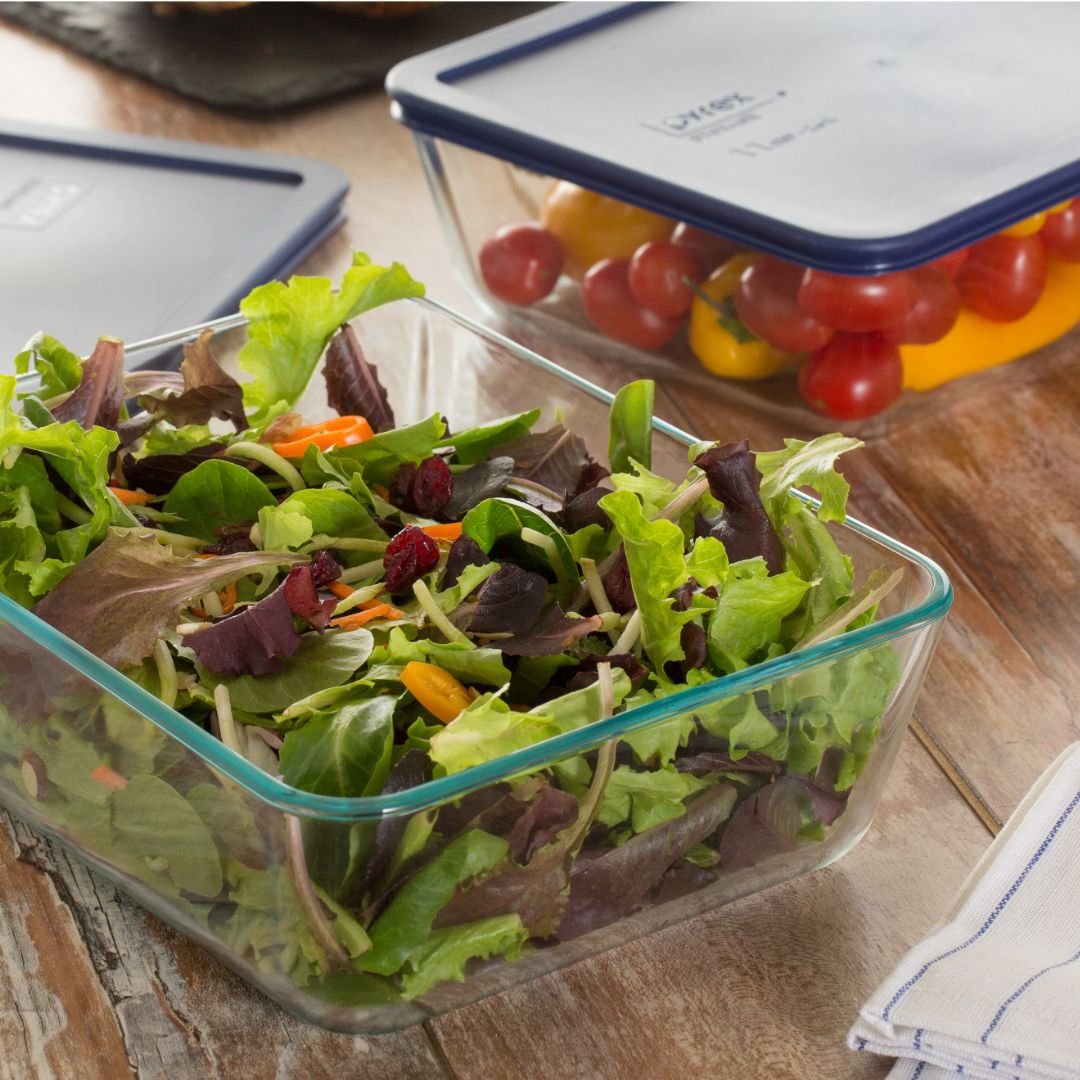 Glass containers with salad and cherry tomatoes on a wooden surface