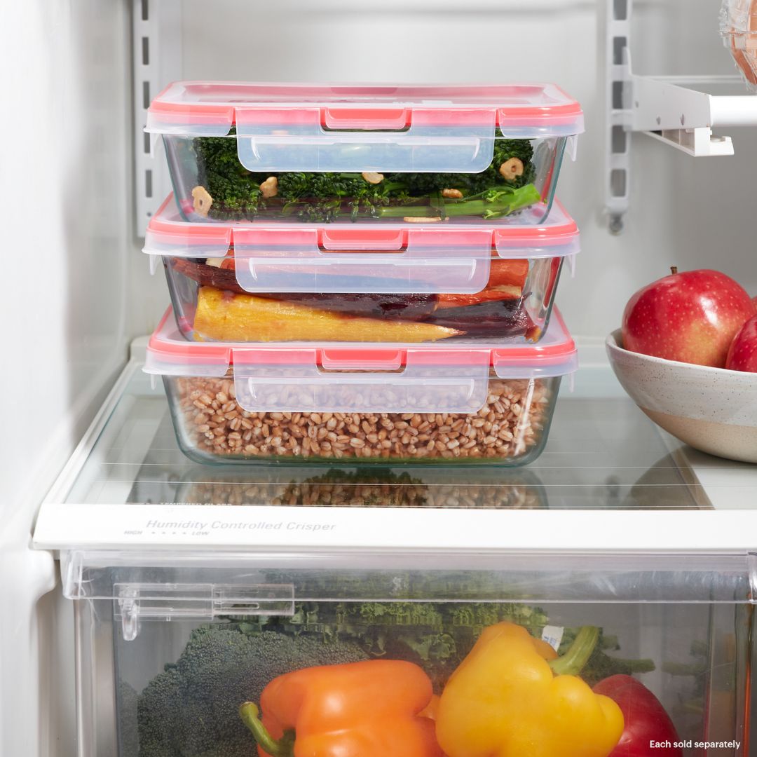 Stack of food storage containers with vegetables inside, placed on a refrigerator shelf.
